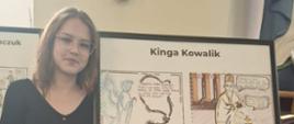 Kinga stoi obok swojej pracy konkursowej czyli komiksu zamieszczonego w szklanej antyramie