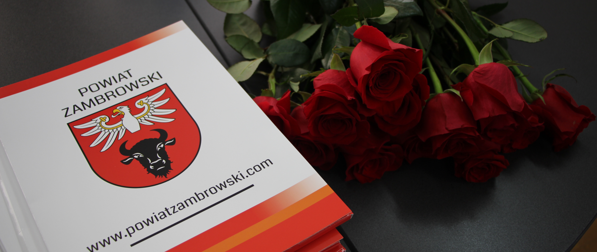 zdjęcia teczek z logo powiatu, a obok czerwone róże