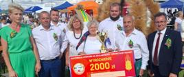 Na zdjęciu członkowie Delegacji Wieńcowej wraz ze starostą, trzymający Voucher nagrodę oraz puchar. W tle wieniec Dożynkowy.