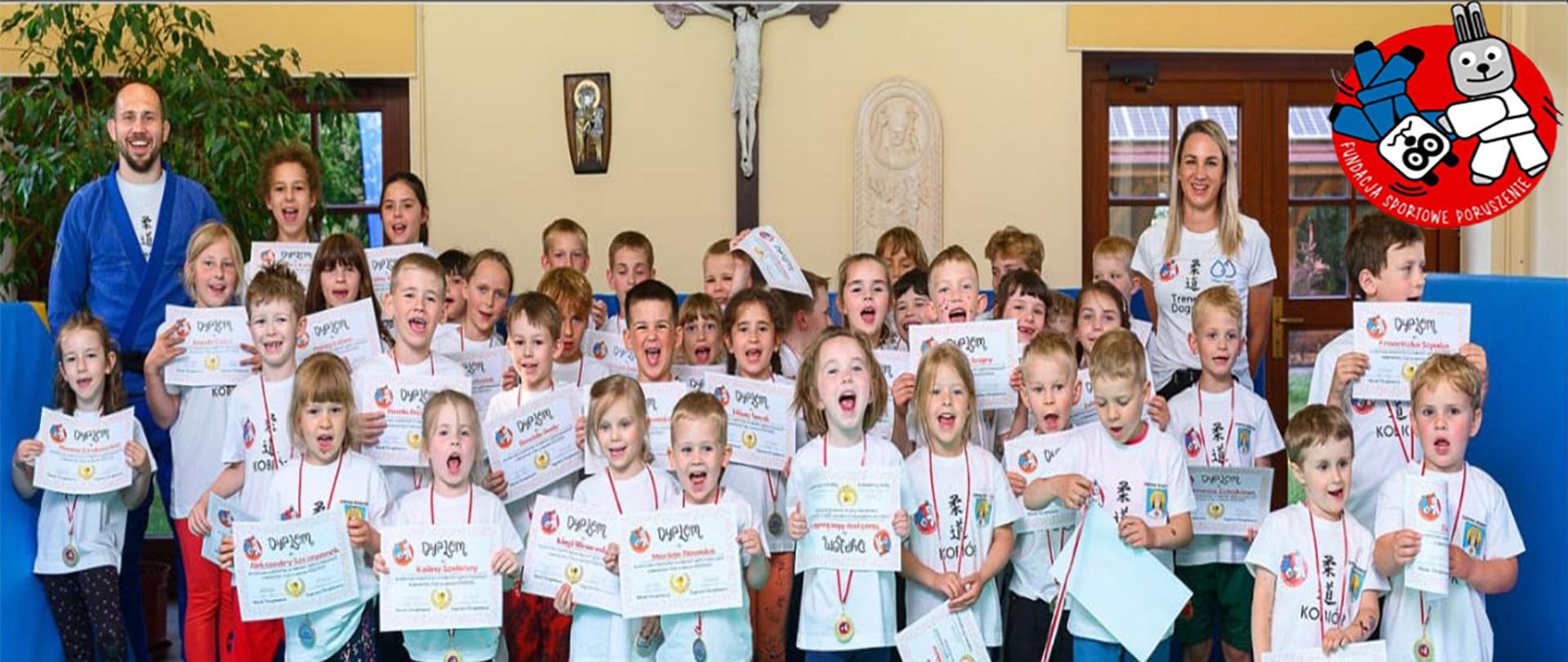 Grupa dzieci z dyplomami z zajęć judo wraz z opiekunami