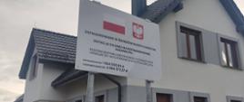 Tablica z informacją o dofinansowaniu. Za nią stoi duży dom.