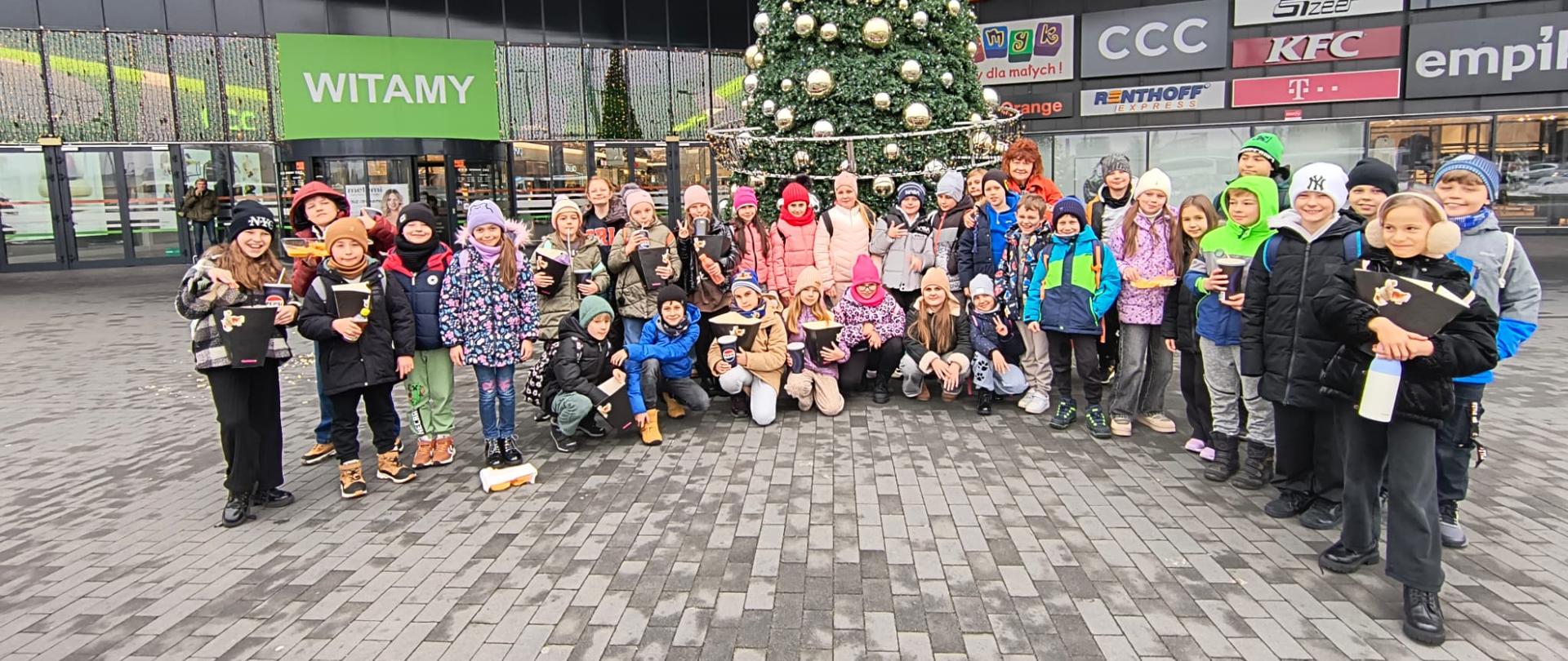 Uczniowie klasy 3a i 3b stoją przed choinką i wejściem do galerii.