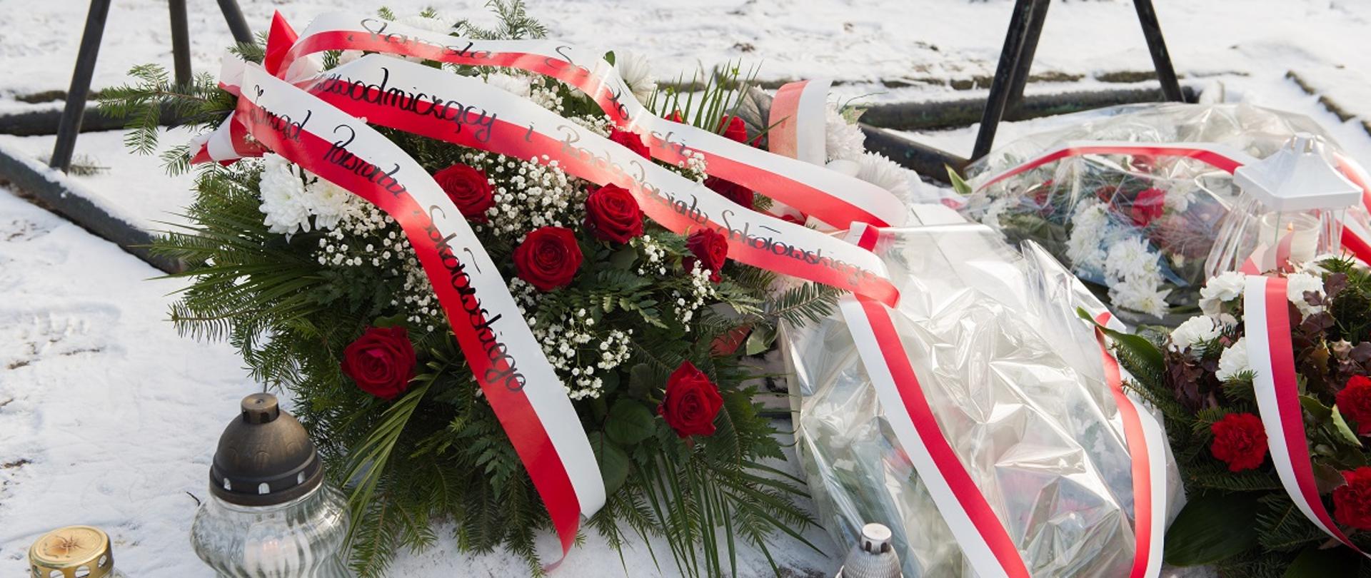 Wiązanką z biało - czerwonych kwiatów na zielonym podkładzie z trzema szarfami w w barwach narodowych z napisami Starosta Sokołowski, Zarząd Powiatu Sokołowskiego, Przewodniczący i Rada Powiatu Sokołowskiego.