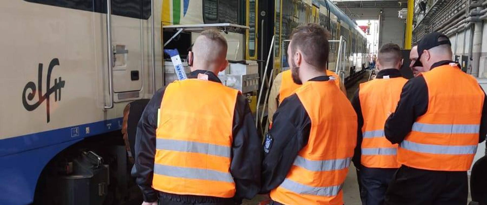 Mężczyźni w pomarańczowych kamizelkach stoją przed pociągiem