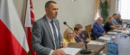 Grafika przedstawia Pana Karola Tchórzewski – Starostę Siedleckiego, który składa podziękowanie Radnym Powiatu Siedleckiego za udzielone absolutorium za rok 2022. Za prezydium od lewej siedzą Pani Małgorzata Cepek – Wicestarosta Siedlecki, Pani Pelagia Piątek – Skarbnik Powiatu, Pan Marek Gorzała – Przewodniczący Rady Powiatu w Siedlcach, Pani Magdalena Paczóska – Wiceprzewodnicząca Rady Powiatu w Siedlcach, Pan Andrzej Rymuza – Sekretarz Powiatu oraz Pan Gracjan Suski – radca prawny