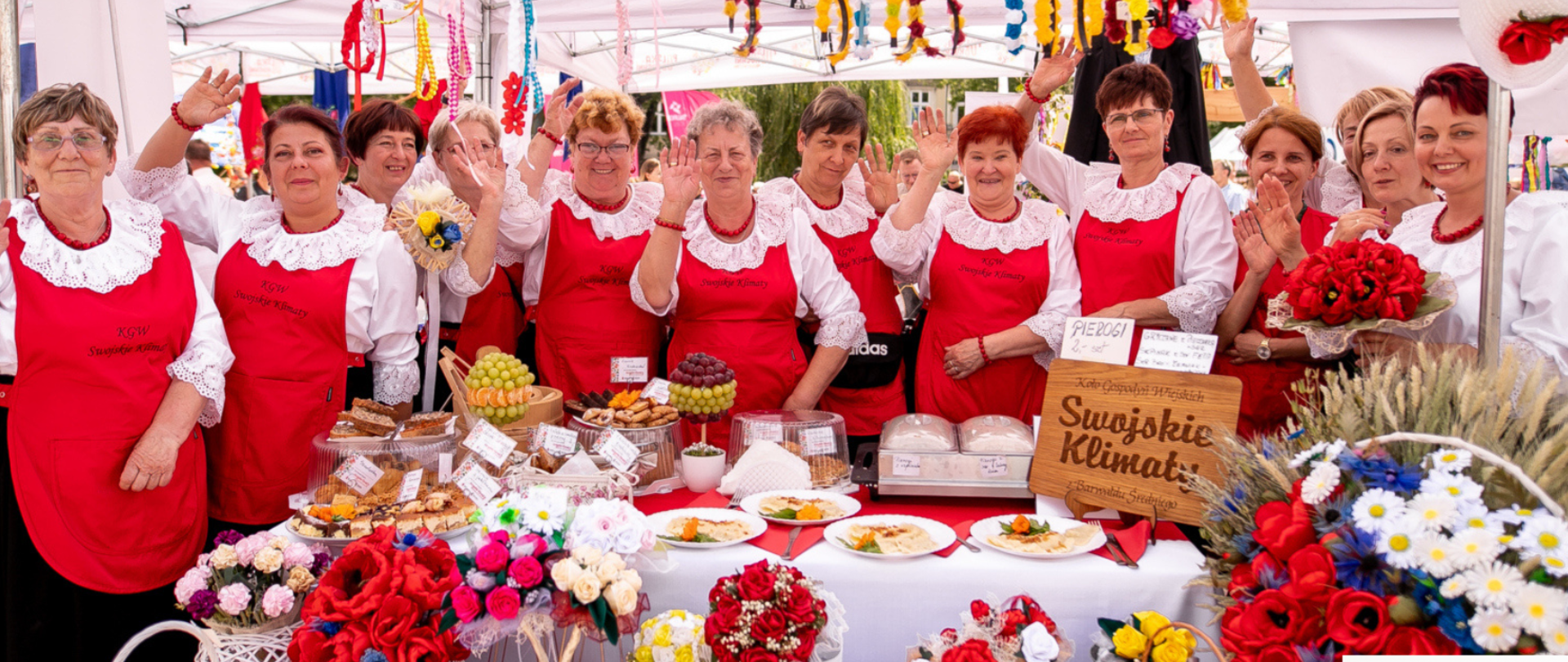 Zdjęcie przedstawiający panie z Kół Gospodyń Wiejskich stojące pod namiotem przy zastawionym stole przekąskami regionalnymi biorący udział w festiwalu „Polska od Kuchni” oraz w prawym rogu logo festiwalu.