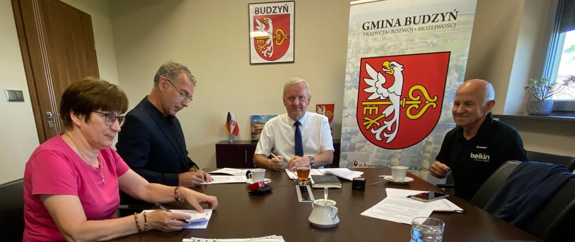 Cztery osoby siedzą przy stole, podpisują dokumenty