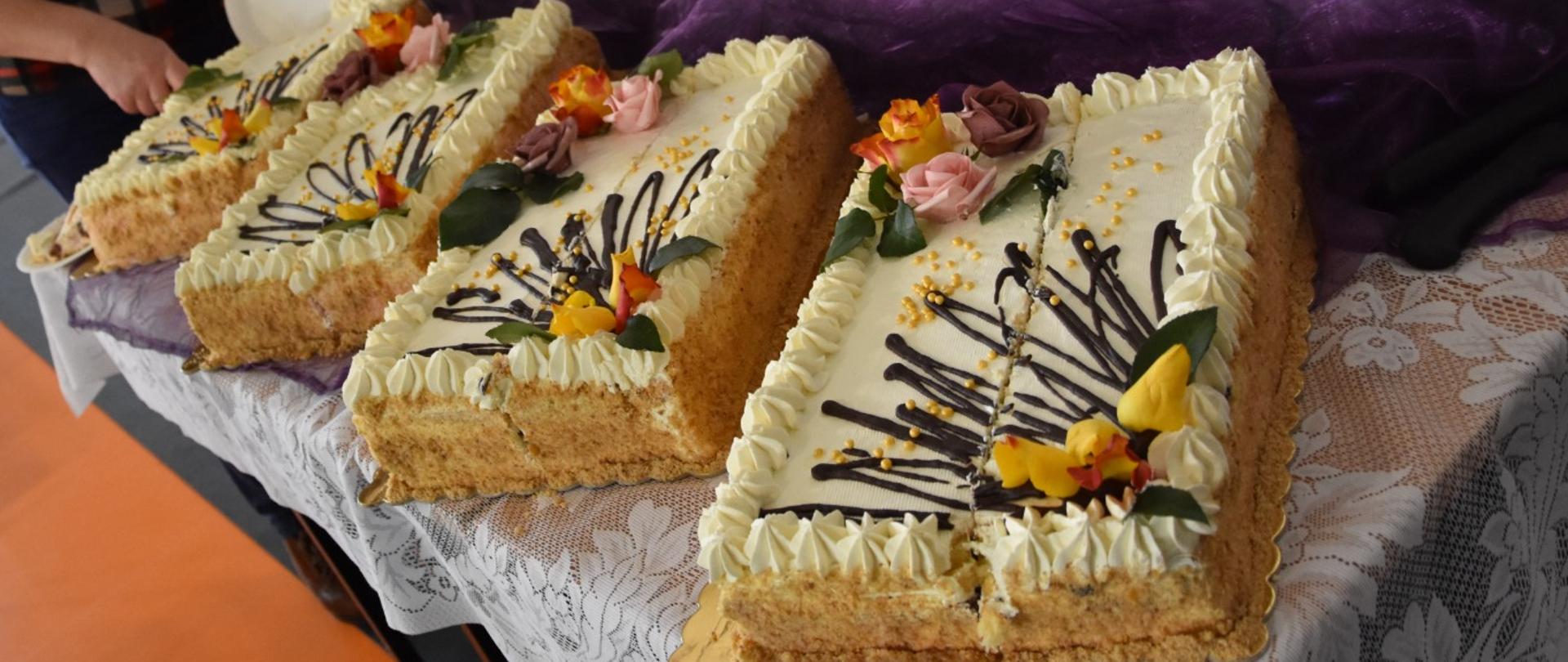 stół, na nim torty przy nich osoba, które je kroi