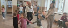 Grupa dzieci z oddziału przedszkolnego znajduje się na korytarzu szkolnym. Maluchy tańczą z Paniami w kółeczku.