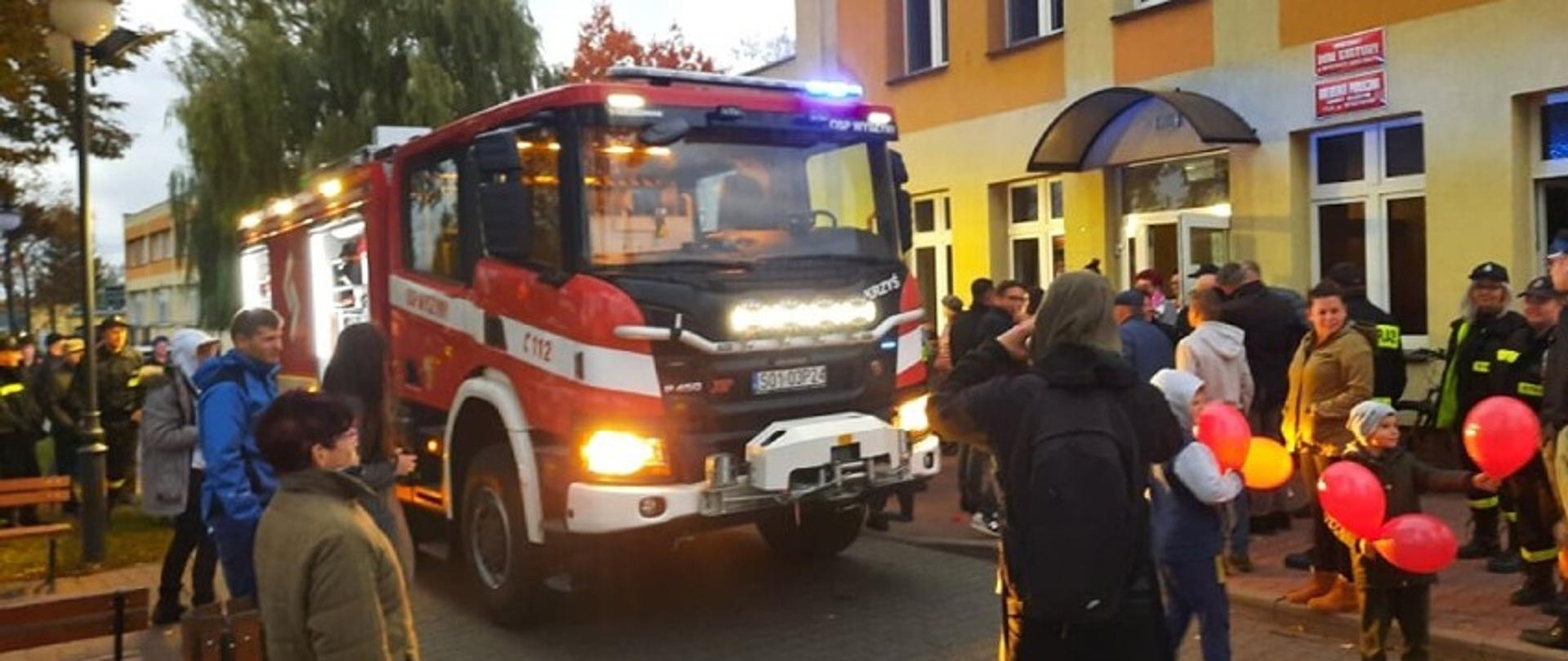 Na zdjęciu widać nowy wóz ratowniczy gaśniczy marki SCANIA oraz mieszkańców wsi Wyszyny, a także strażaków z jednostek OSP z terenu Gminy Budzyń, którzy fotografują oraz oglądają pojazd.