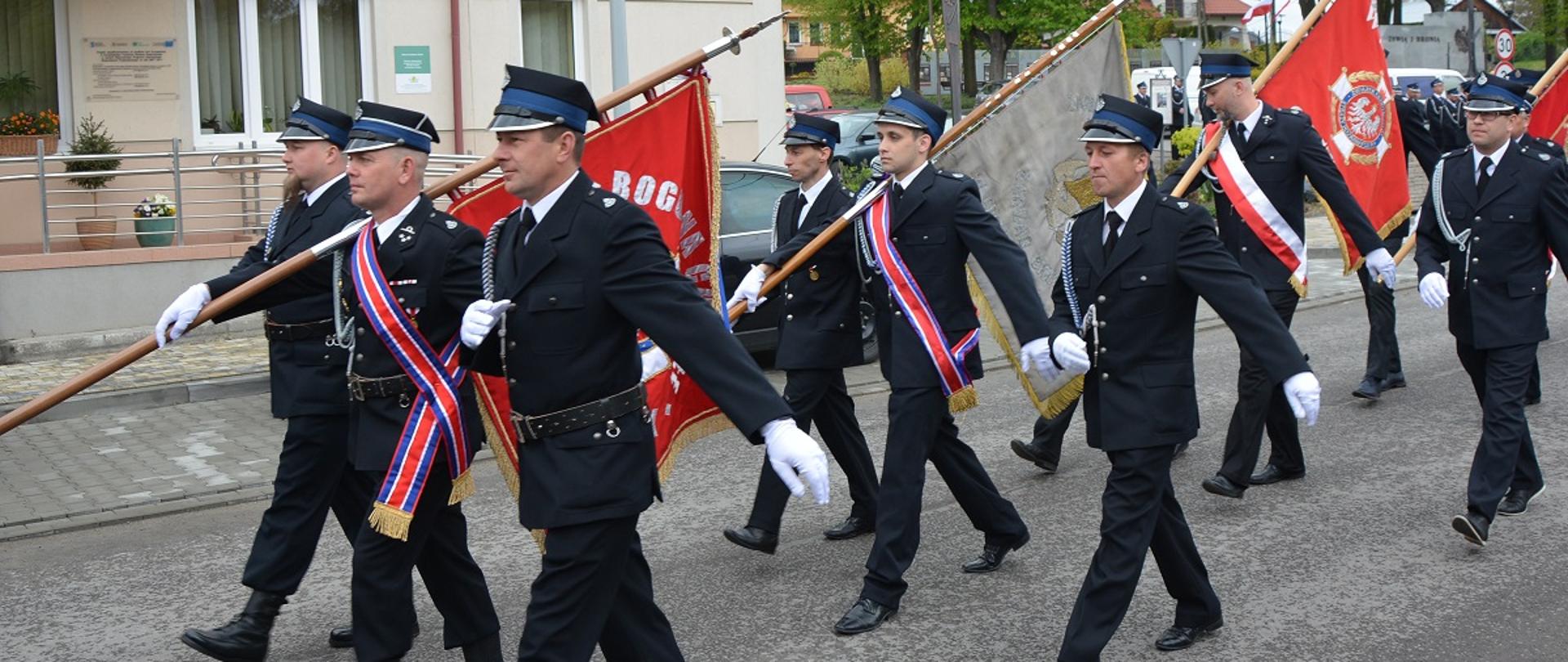 Mężczyźni ubrani w ciemne mundury i czapki z sztandarami idą w pochodzie 