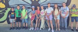 Grupa uczniów stoi na tle muralu z motylem.
