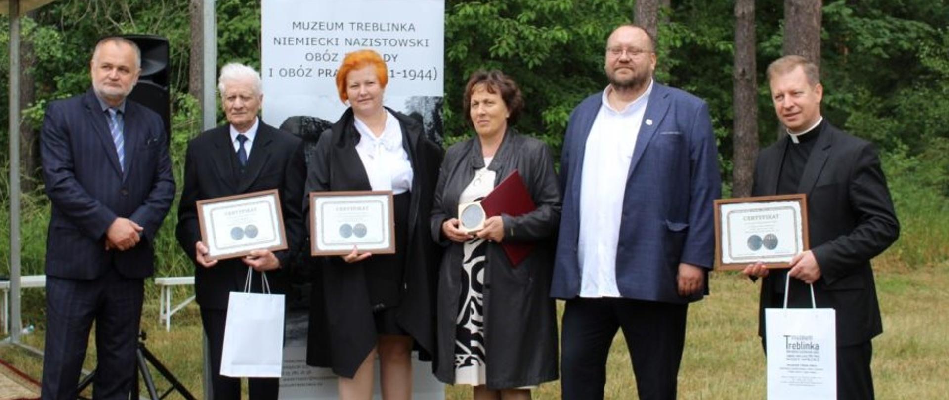 Zdjęcie grupowe na tle lasu osób oraz instytucji uhonorowanych medalem Zasłużony dla Muzeum Treblinka. Wraz z wyróżnionymi na zdjęciu dyrektor Muzeum.