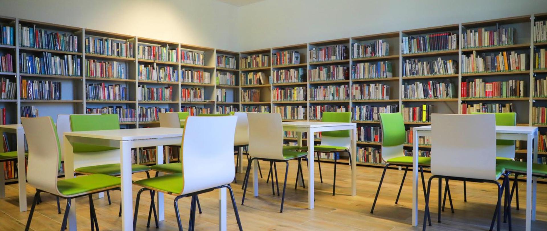 Biblioteka z półkami pełnymi książek oraz stolikami i krzesłami