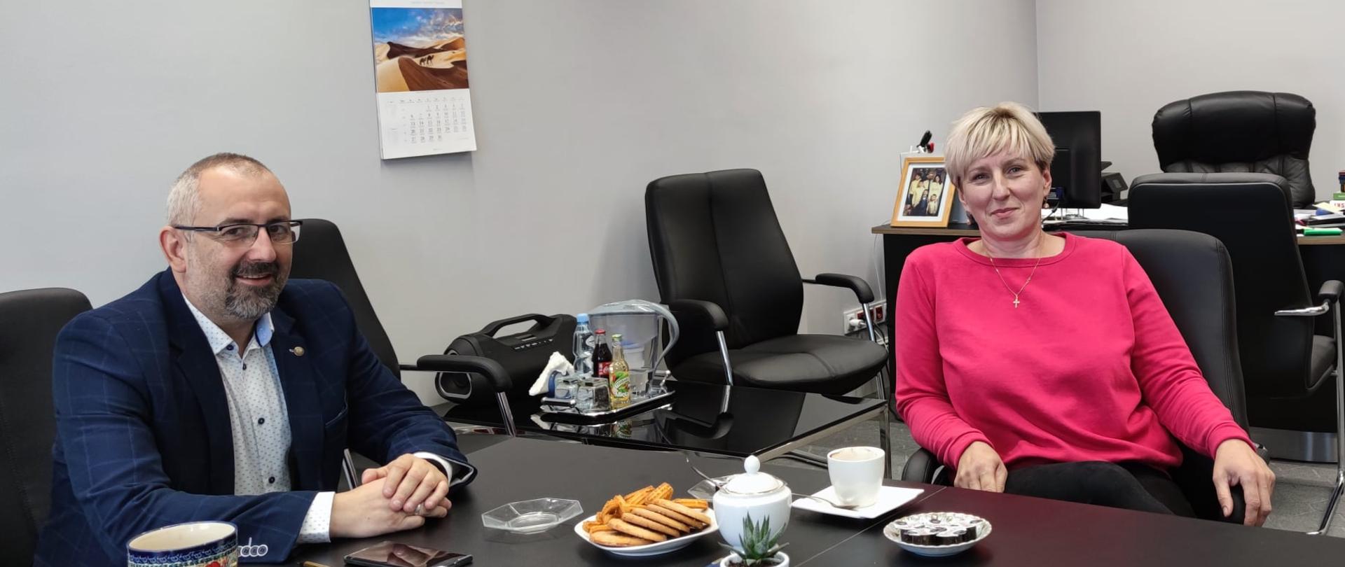 Zdjęcie przedstawia prowadzących rozmowę przy stole Starostę Przasnyskiego Krzysztofa Bieńkowskiego (po lewej) i Hannę Berk (po prawej). Zdjęcie wykonano w gabinecie Starosty Przasnyskiego. 