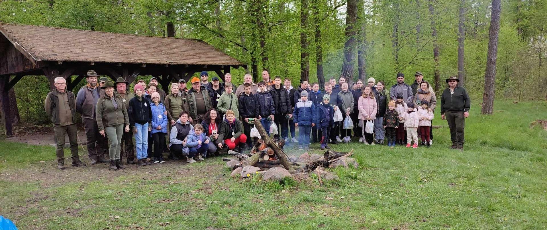 Zdjęciu wszystkich uczestników akcji przy ognisku w tle las oraz altana 