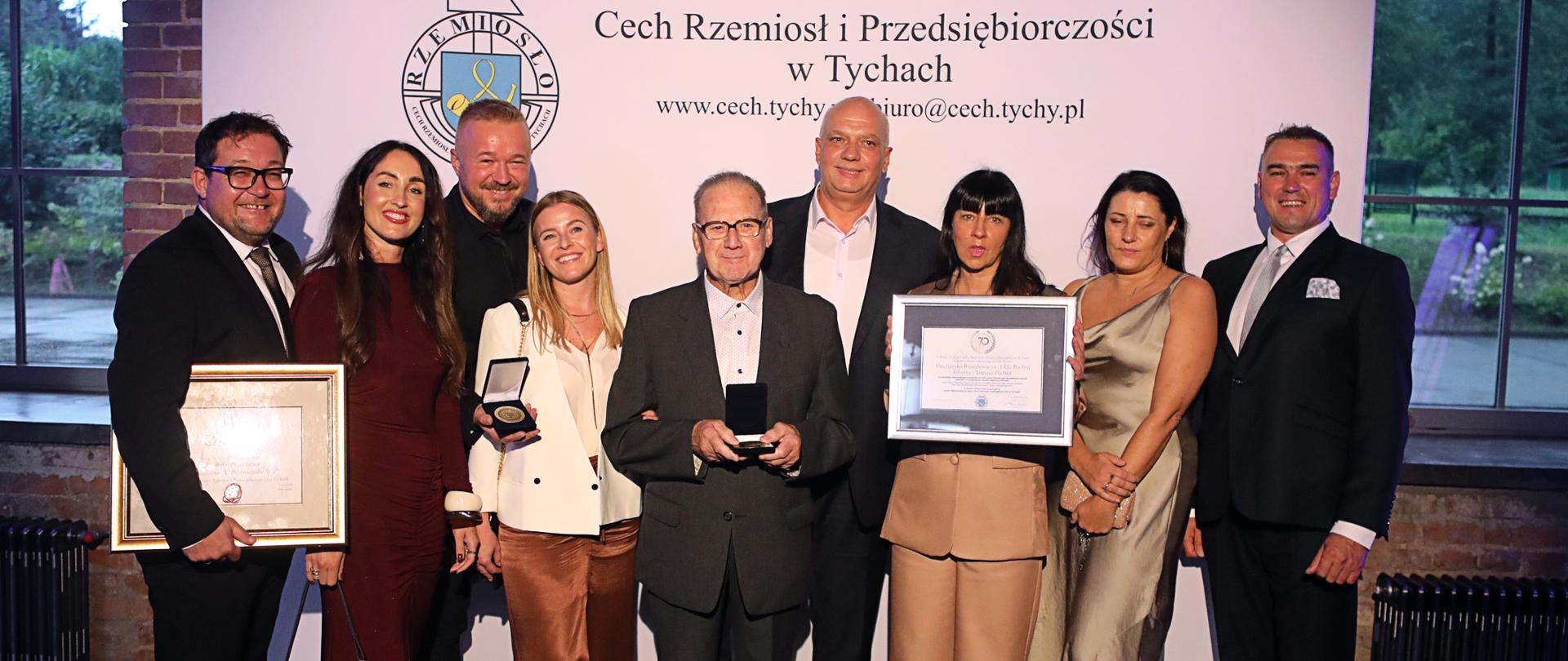 Grupa ludzi pozuje do zdjęcia pod banerem Cech
