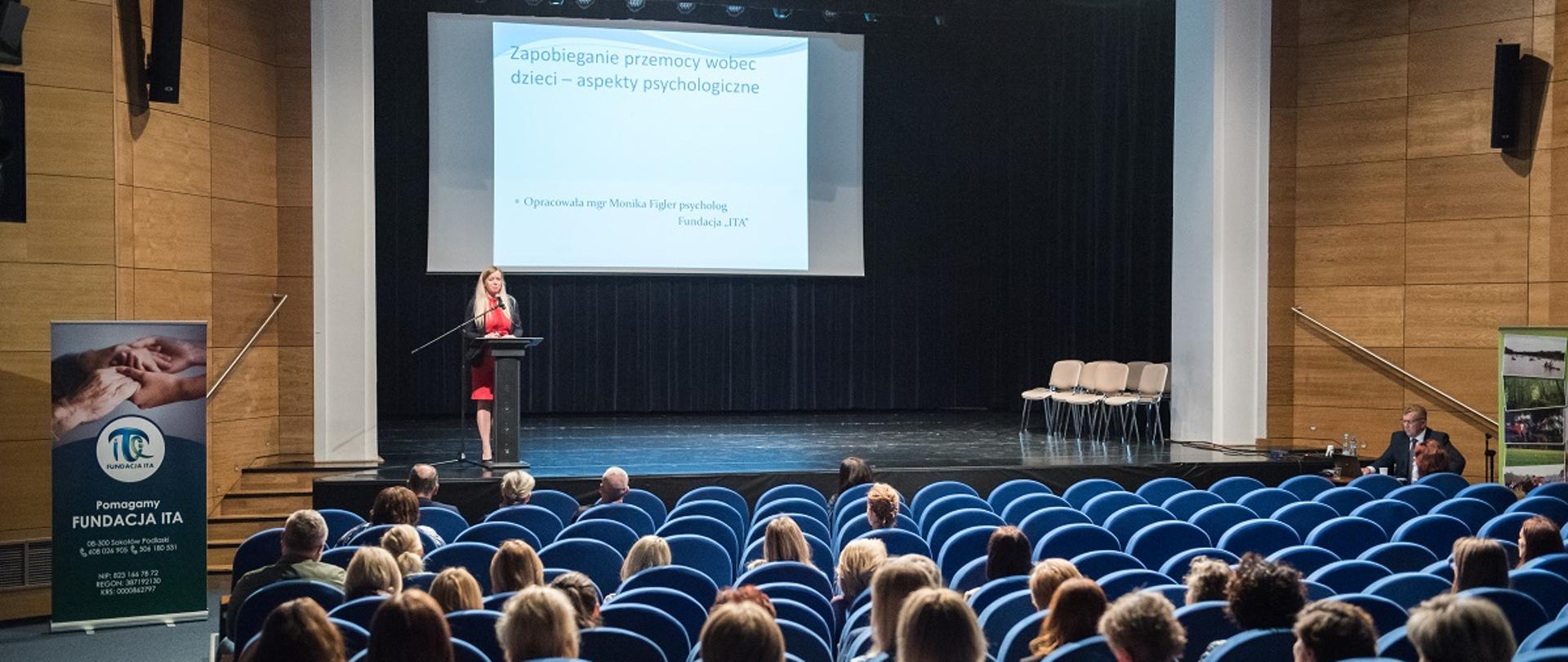 Rzut ogólny na salę widowiskową Sokołowskiego Ośrodka Kultury. W poszczególnych rzędach siedzą uczestnicy. Na scenie jeden z prelegentów. Na ekranie w głębi sceny slajd pt. Zapobieganie przemocy wobec dzieci - aspekty psychologiczne.