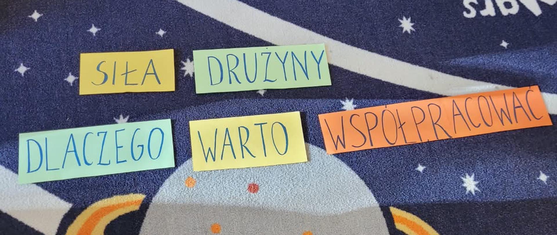 Na górze zdjęcia granatowe tło z fragmentami białych linii. Z prawej strony czerwone koło przecinające białą linię. Pośrodku zdjęcia wyrazy ułożone w dwóch liniach, zapisane na kolorowych kartkach. Poniżej nich koło w kolorze błękitnym wraz z otoczką wokół w kolorze żółtym. W lewym dolnym rogu fragment sywetki osoby. Na dole zdjęcia biały napis na granatowym tle.