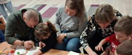 Rodzice z dziećmi siedzą przy stole, przygotowują gwiazdy z papieru