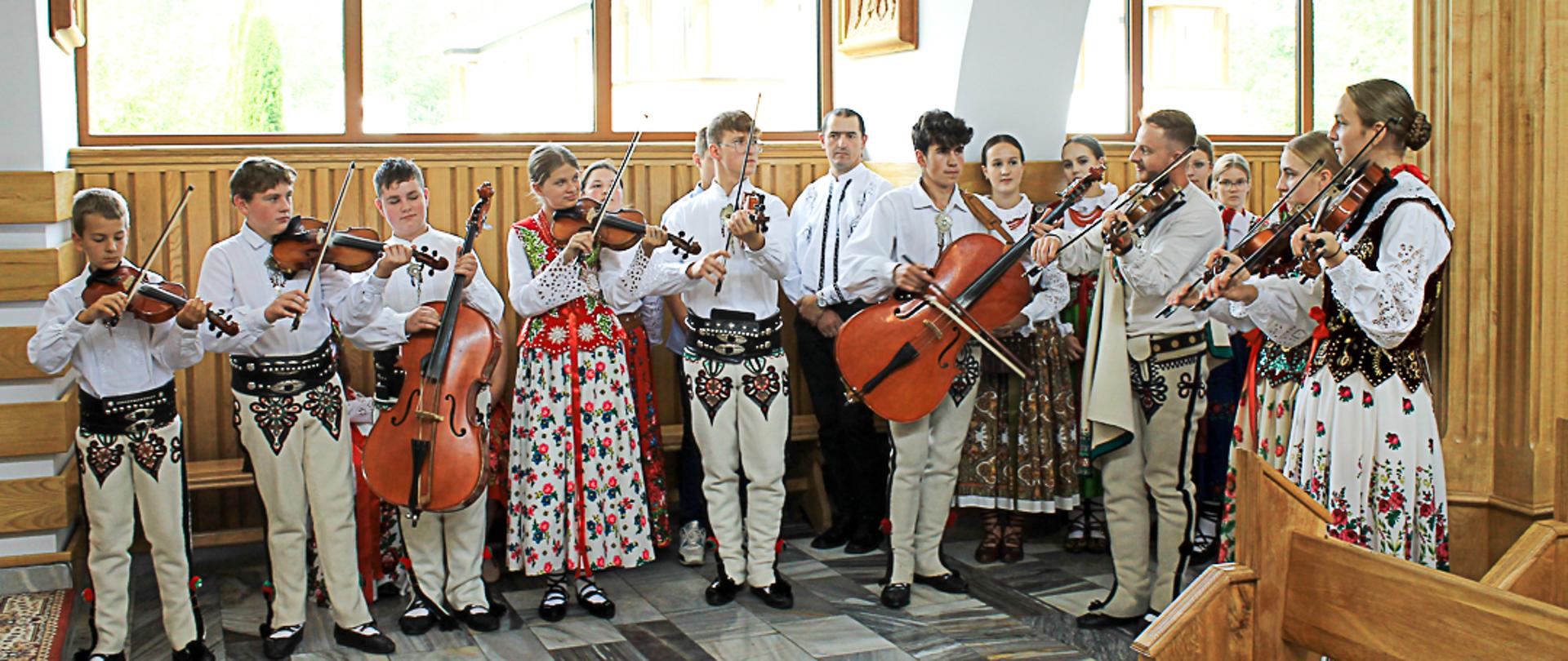 Zespół góralski ubrany w stroje regionalne grający na skrzypcach i basach stojący w kościele