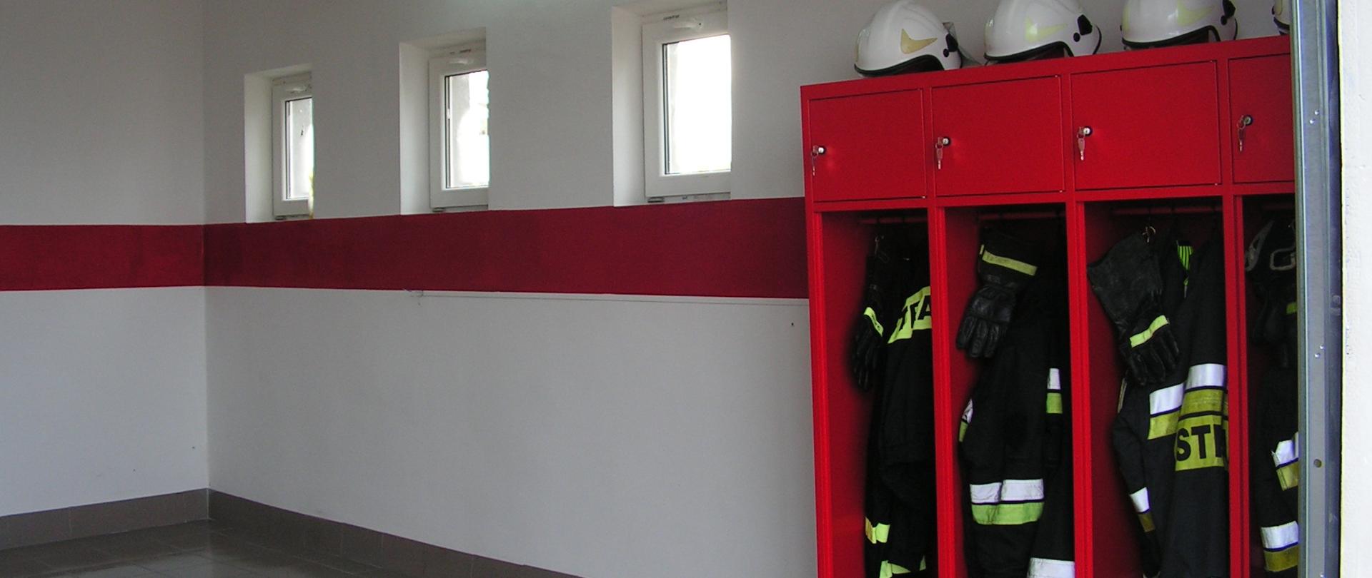 Na zdjęciu przedstawiono jedno z wyremontowanych pomieszczeń strażnicy OSP Jonne i OSP Chromakowo. Dominują kolory bieli i czerwieni. W prawym rogu mieści się czerwona szafa z ubraniami strażaków. Miejsce jest czyste i nowoczesne.