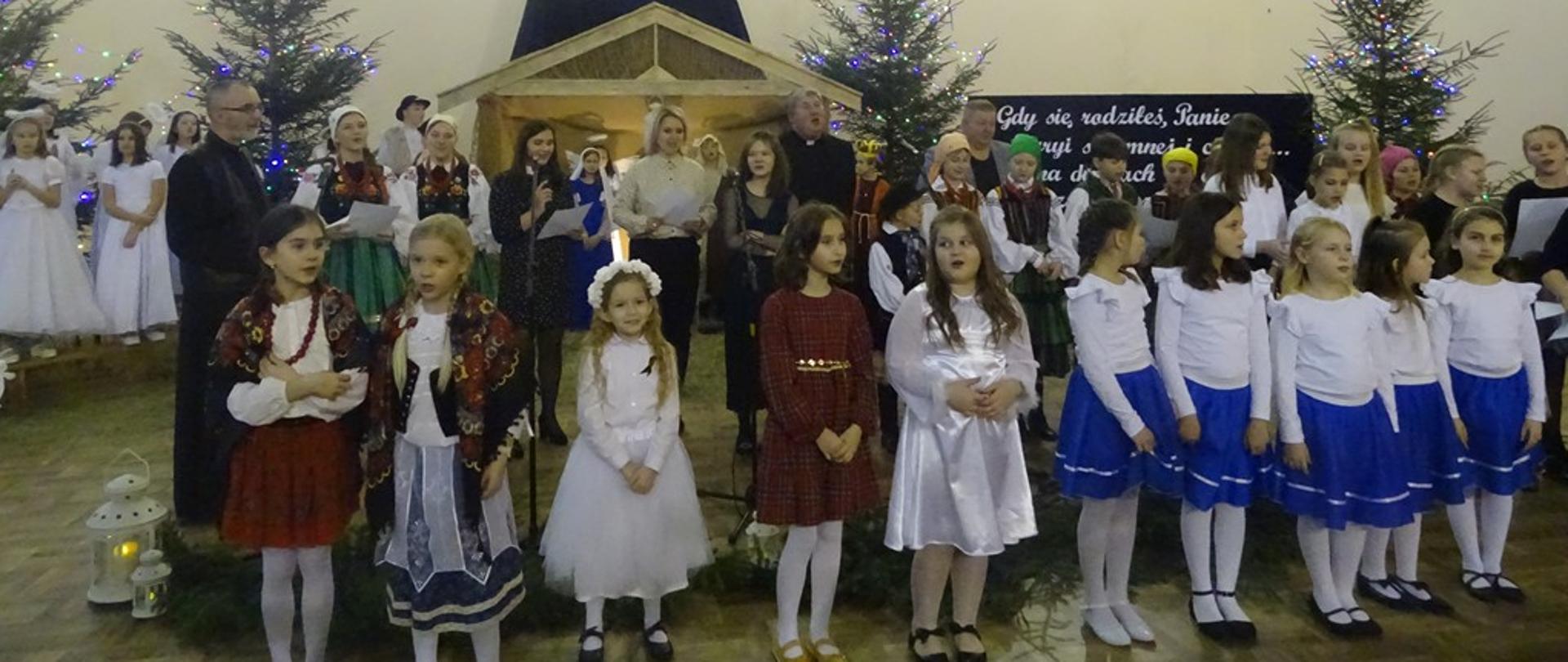 Zdjęcie przedstawia wszystkich uczestników, organizatorów oraz księży, którzy odśpiewują utwór na zakończenie Gminnego Przeglądu Kolęd i Pastorałek. 