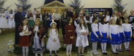 Zdjęcie przedstawia wszystkich uczestników, organizatorów oraz księży, którzy odśpiewują utwór na zakończenie Gminnego Przeglądu Kolęd i Pastorałek. 