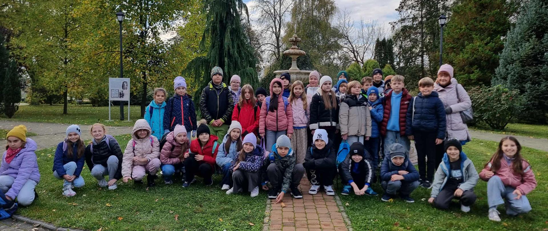 Grupa dzieci z dwóch klas 3a I 3b, ustawione w trzech rzędach, stojące przed fontanną Pałacyku Oborskich. 