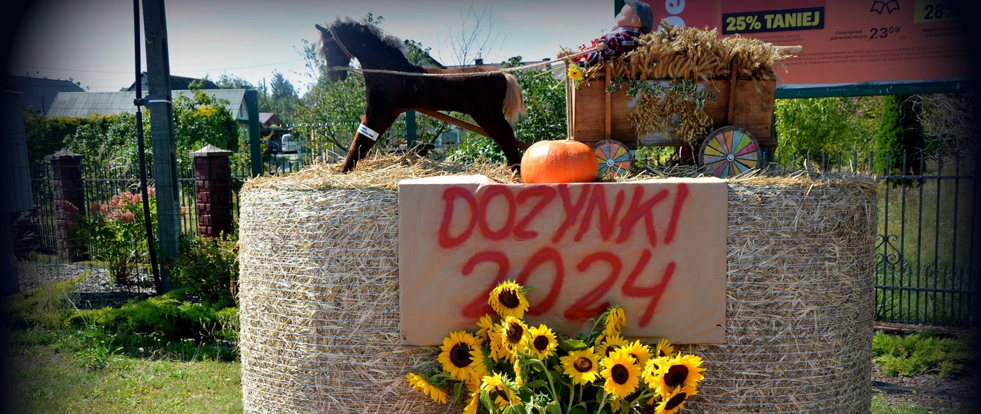 dwa duże okrągłe bele siana na nich koń z wozem i napis dożynki 2024pod spodem słoneczniki i dynie 