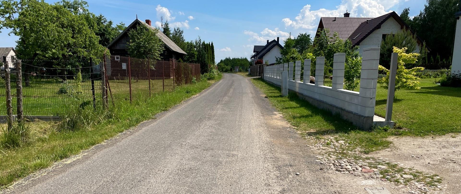 Droga gminna po obu stronach znajdują się ogrodzenia i zabudowania.