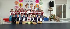 Dzieci w strojach śląskich wraz z dorosłymi paniami pozują do zdjęcia w jasnej sali