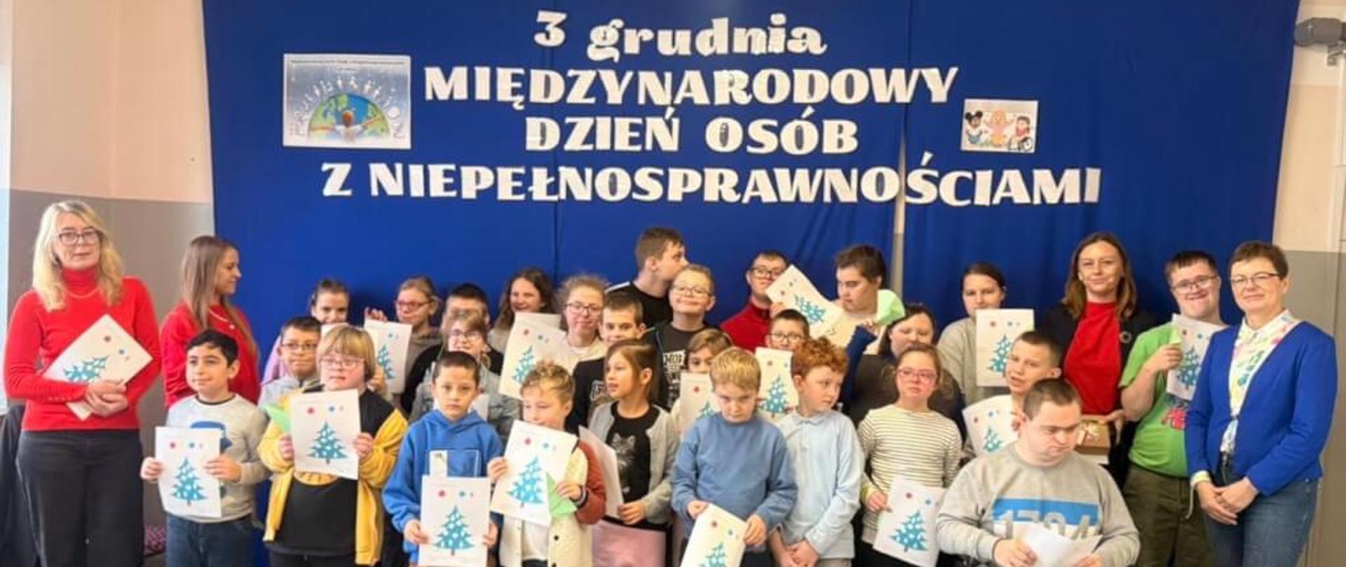 Zdjęcie przedstawia grupę dzieci ze szkoły specjalnej w Konstantynowie Łódzkim. Zdjęcie zostało zrobione z okazji Międzynarodowego Dnia Osób z Niepełnosprawnościami