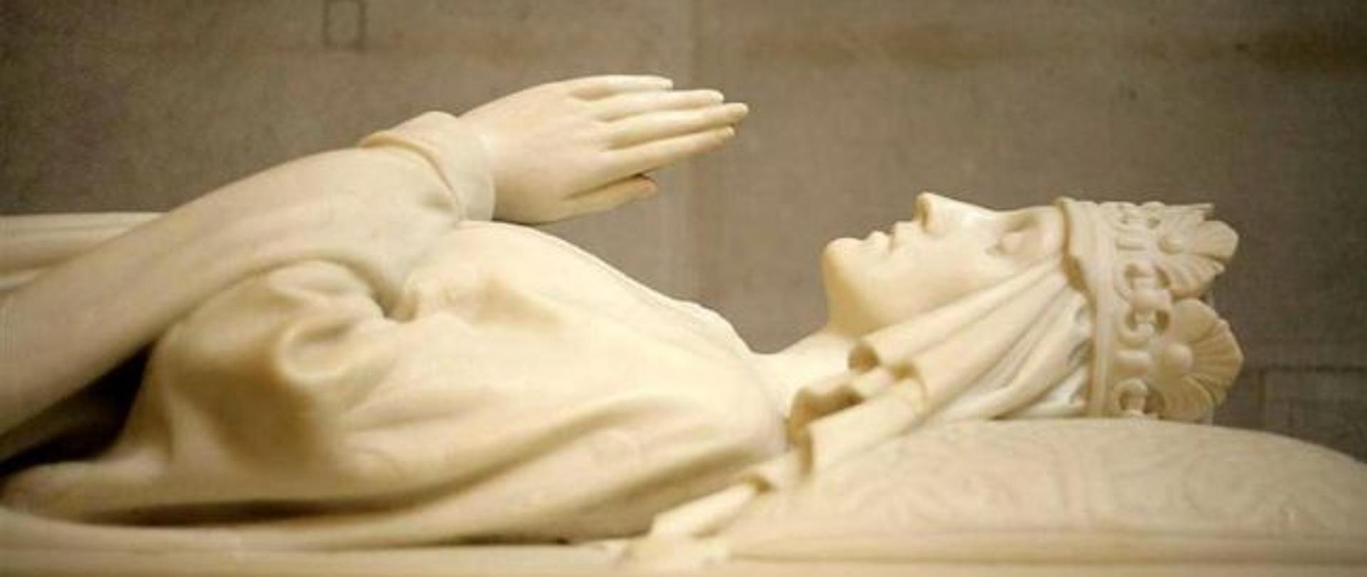 Postać leżącej kobiety z koroną na głowie i złożonymi rękoma do modlitwy wyrzeźbiona w marmurze