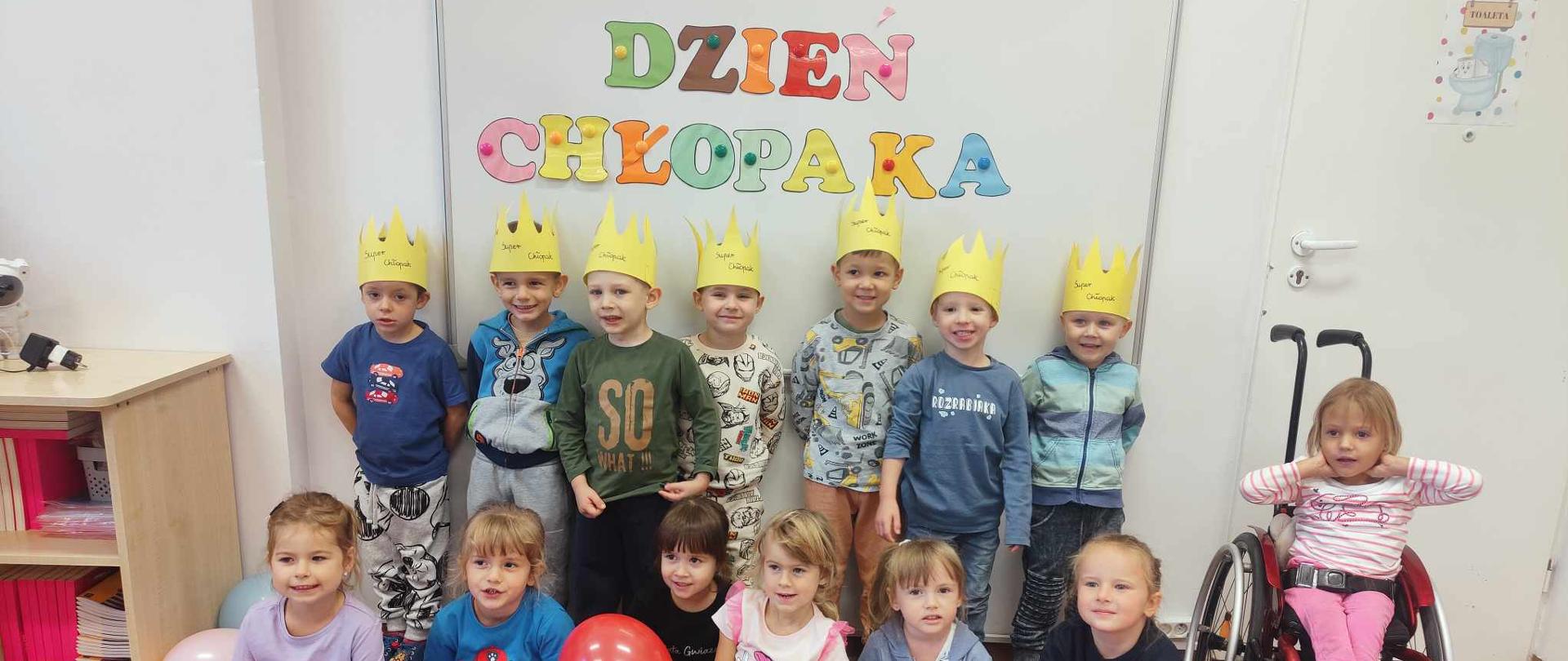 Grupa uśmiechniętych przedszkolaków na tle napisu „Dzień Chłopaka”. Chłopcy mają założone na głowach korony.