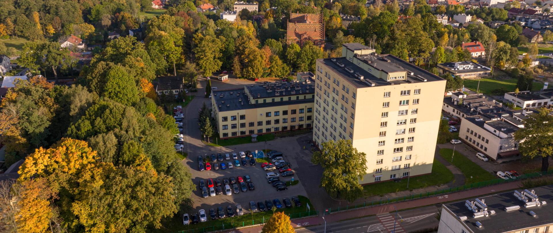 Jasny budynek szpitala w Pszczynie, w tle zabudowania oraz tereny zadrzewione