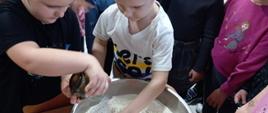 Warsztaty kulinarne - dzieci stoją przy stole ze składnikami, chłopiec miesza mąkę