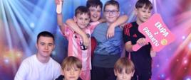 4 chłopców stoi przy fotościance przedstawiającej niebo i gwiazdy, jeden chłopiec trzyma w ręku napis "Królowa parkietu", chłopieć po prawej stronie trzyma napis "Ekipa z parkietu", przed nimi kuca jeszcze 3 chłopców