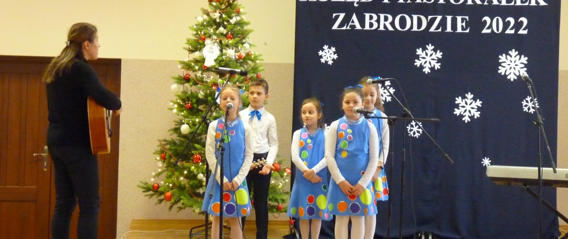 Dzieci ubrane na niebiesko śpiewają na scenie