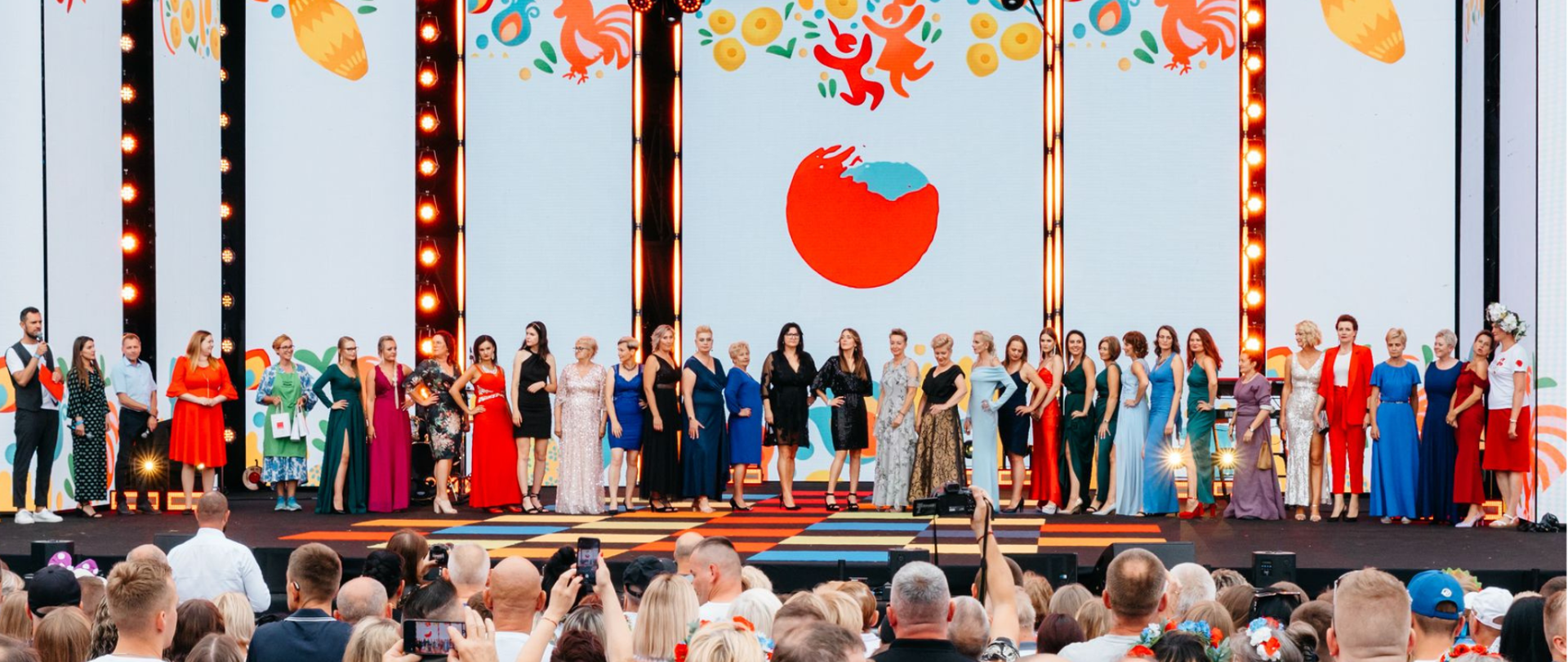 Zdjęcie przedstawiający kandydatki na scenie przed publicznością startujące do Wybory Miss Wdzięku podczas Festiwalu „Polska Od Kuchni”z ubiegłego roku oraz w prawym rogu logo festiwalu.