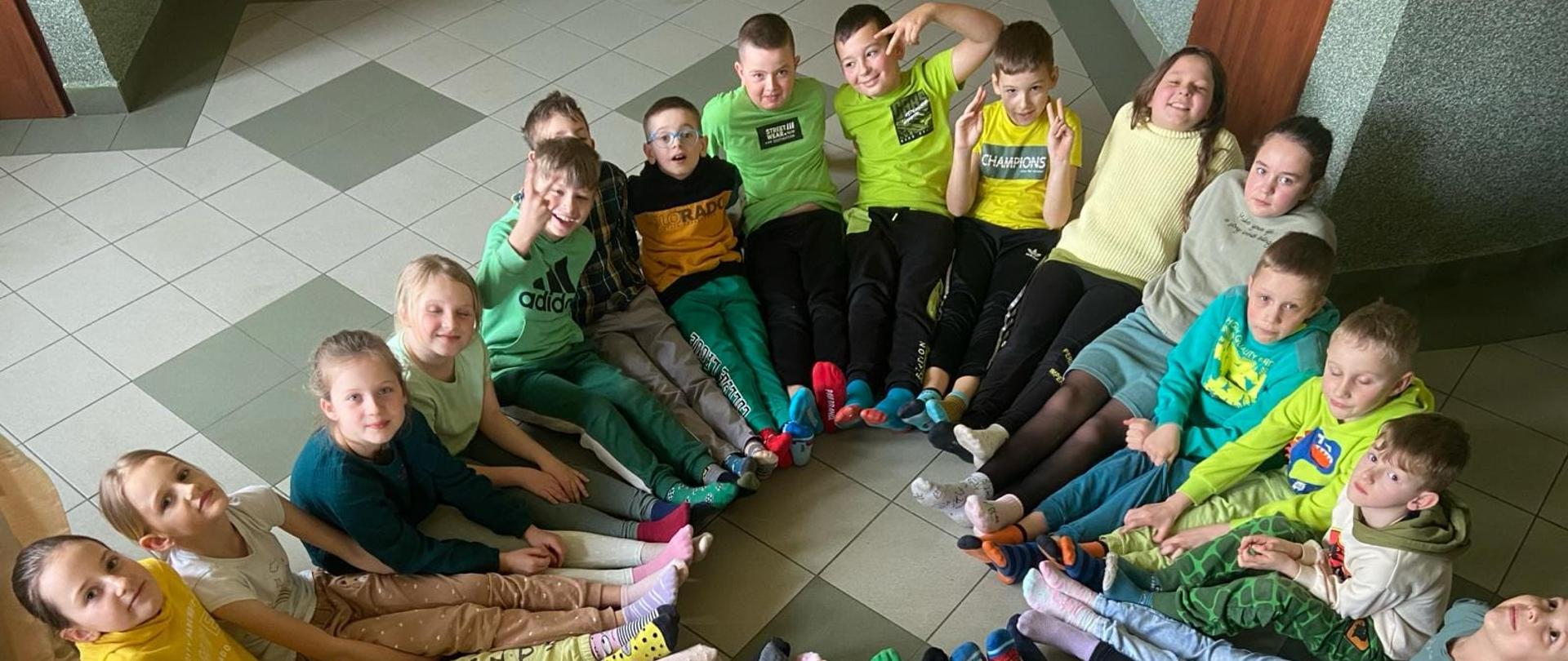 Uczniowie w kolorowych skarpetkach siedzą w kole, z wyprostowanymi nogami, stykają się stopami tworząc w ten sposób kolorowe koło 