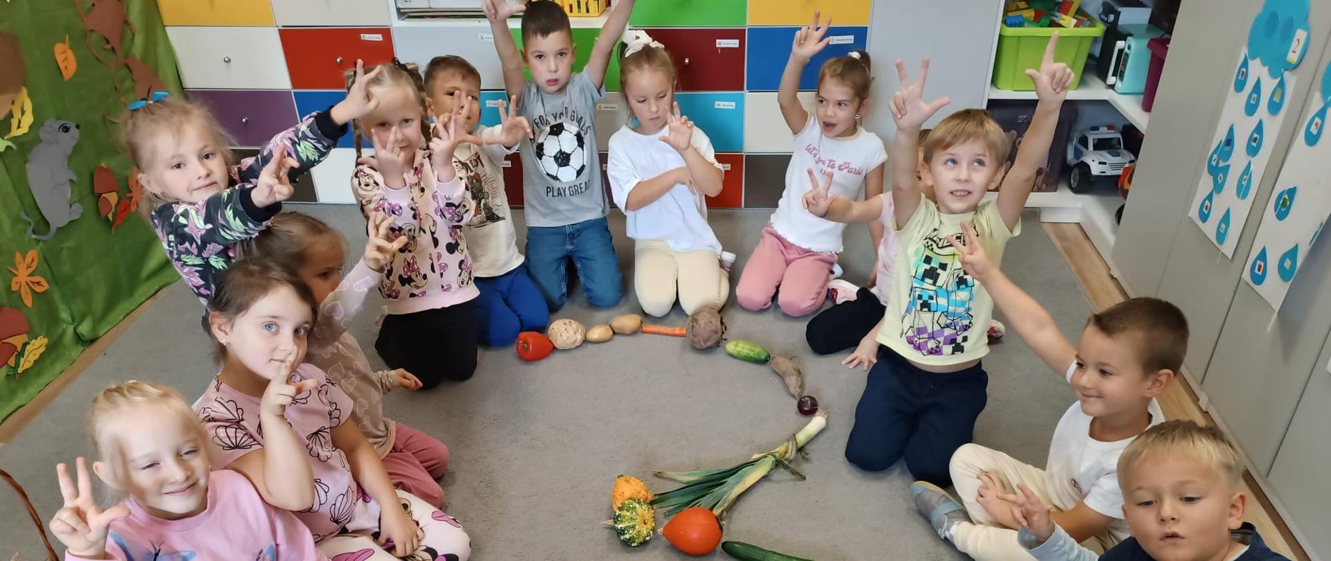 Dzieci siedzą na dywanie. Przed nimi serce ułożone z różnych warzyw i owoców.