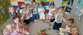 Dzieci siedzą na dywanie. Przed nimi serce ułożone z różnych warzyw i owoców.