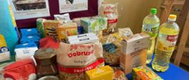 Zebrane przez dzieci dary żywnościowe na stoliku, między innymi makarony, cukier, ryż, oleje