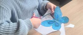 Dziewczynka wycina niebieskiego motyla z papieru
