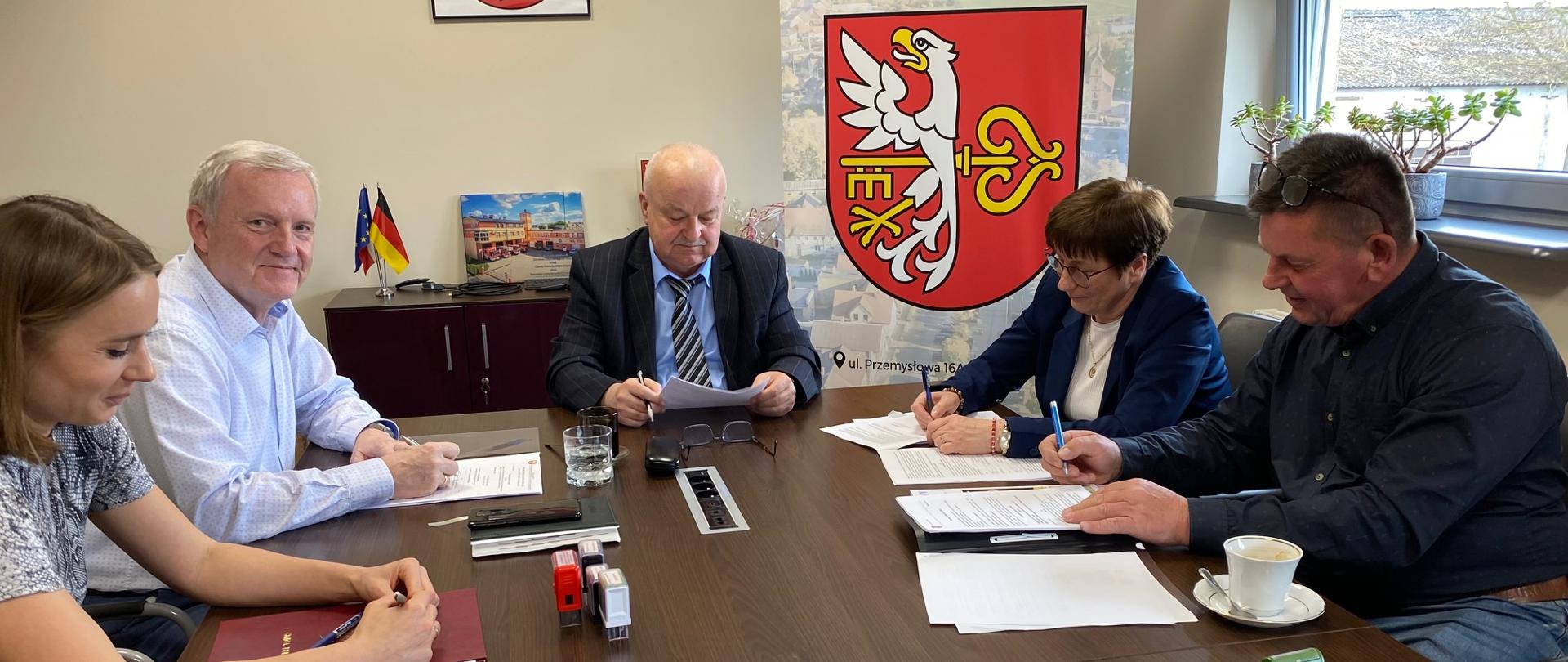 Pięć osób siedzących przy stole, podpisujących dokumenty