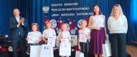4 dziewczynki w białych bluzkach trzymające papierowe białe torby, obok nich mężczyzna i 2 kobiety
