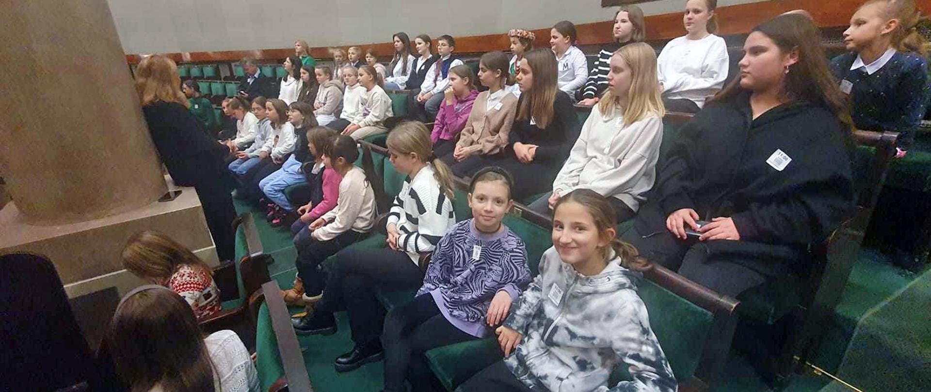 Grupa dzieci siedząca na zielonych krzesłach w Sejmie