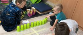 Matematyczne zabawy - dzieci siedzą przed drabiną sklejoną z taśmy na podłodze. 