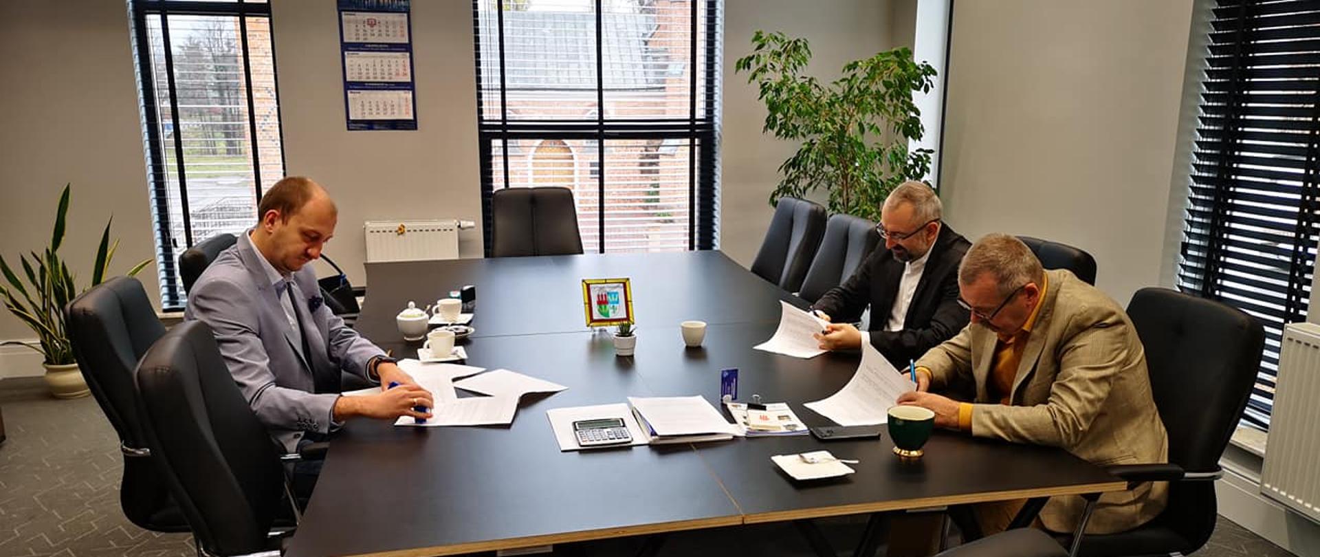Zdjęcie przedstawia od lewej: Burmistrz Przasnysza Łukasz Chrostowski, Starosta Przasnyski Krzysztof Bieńkowski, Wicestarosta Przasnyski Waldemar Trochimiuk podpisują umowę udzielenia Miastu przez Powiat Przasnyski dotacji na zakup kamer wspierających system monitoringu miejskiego. Zdjęcie wykonano w gabinecie Starosty Przasnyskiego w dniu 3 listopada 2021.